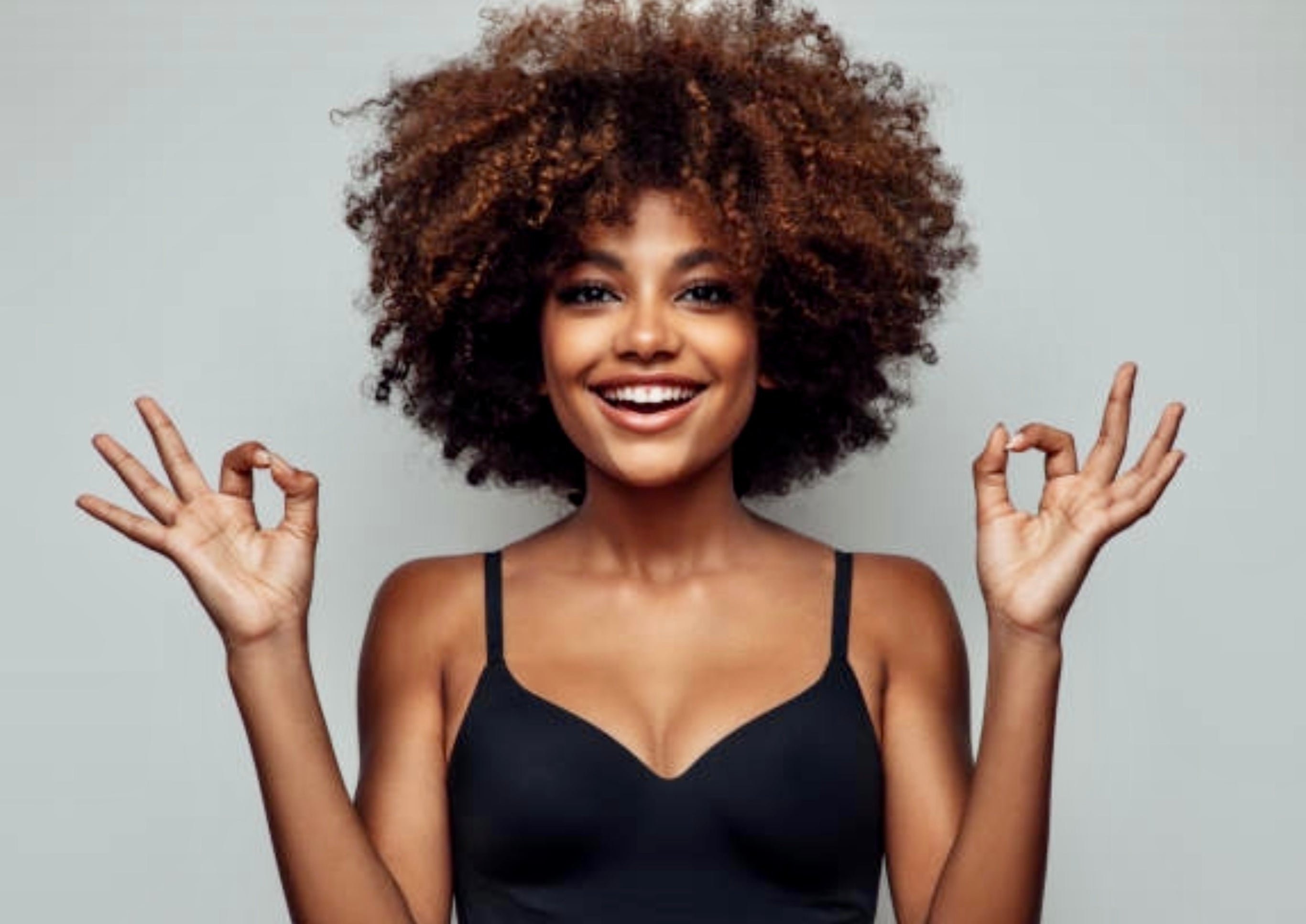 Female model with bouncy curly hair smiling posing at camera with both hands gesturing okay symbol 
