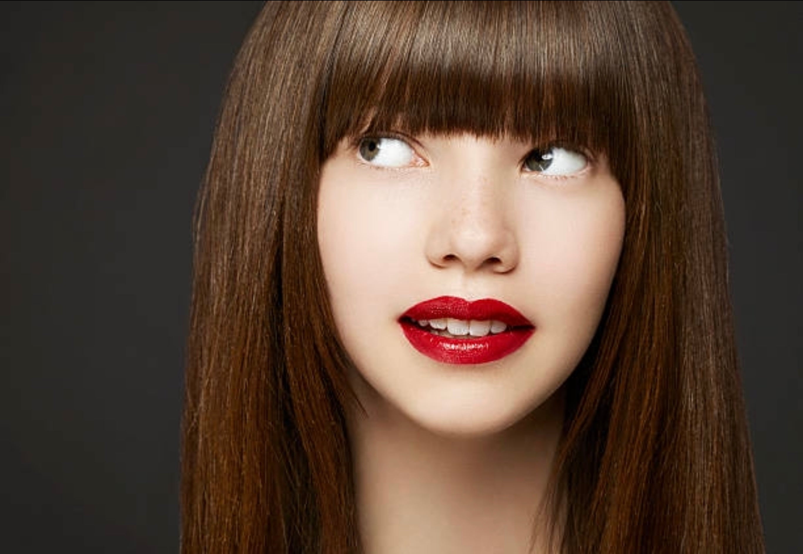 Model with red lipstick long brown hair and fringe looking to the corner of her eyes posing for photoshoot