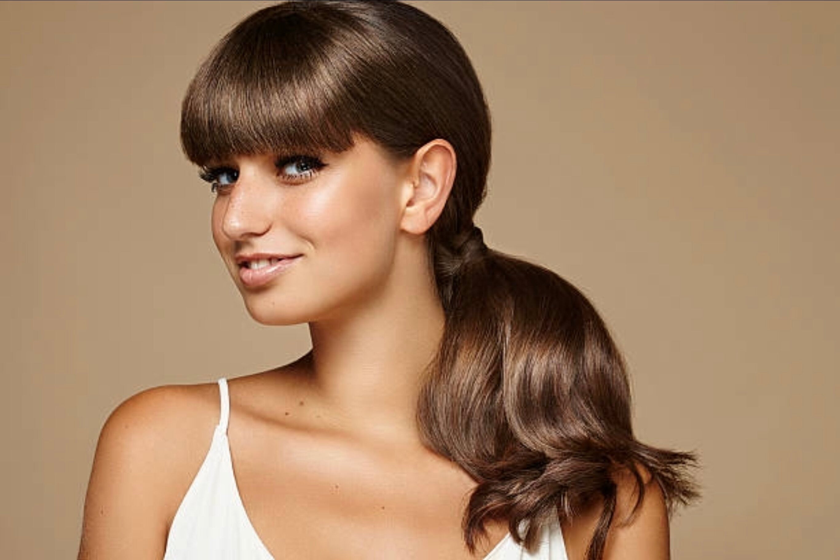 Female model with fringe and shoulder length hair standing with head titled to the left smiling posing for photoshoot